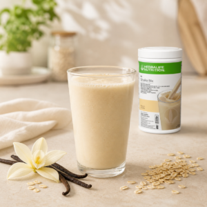 Segelas shake French Vanilla dengan kemasan Herbalife Formula 1, bunga vanila, dan oat di atas meja.
